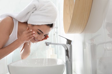 Happy young woman washing face in bathroom