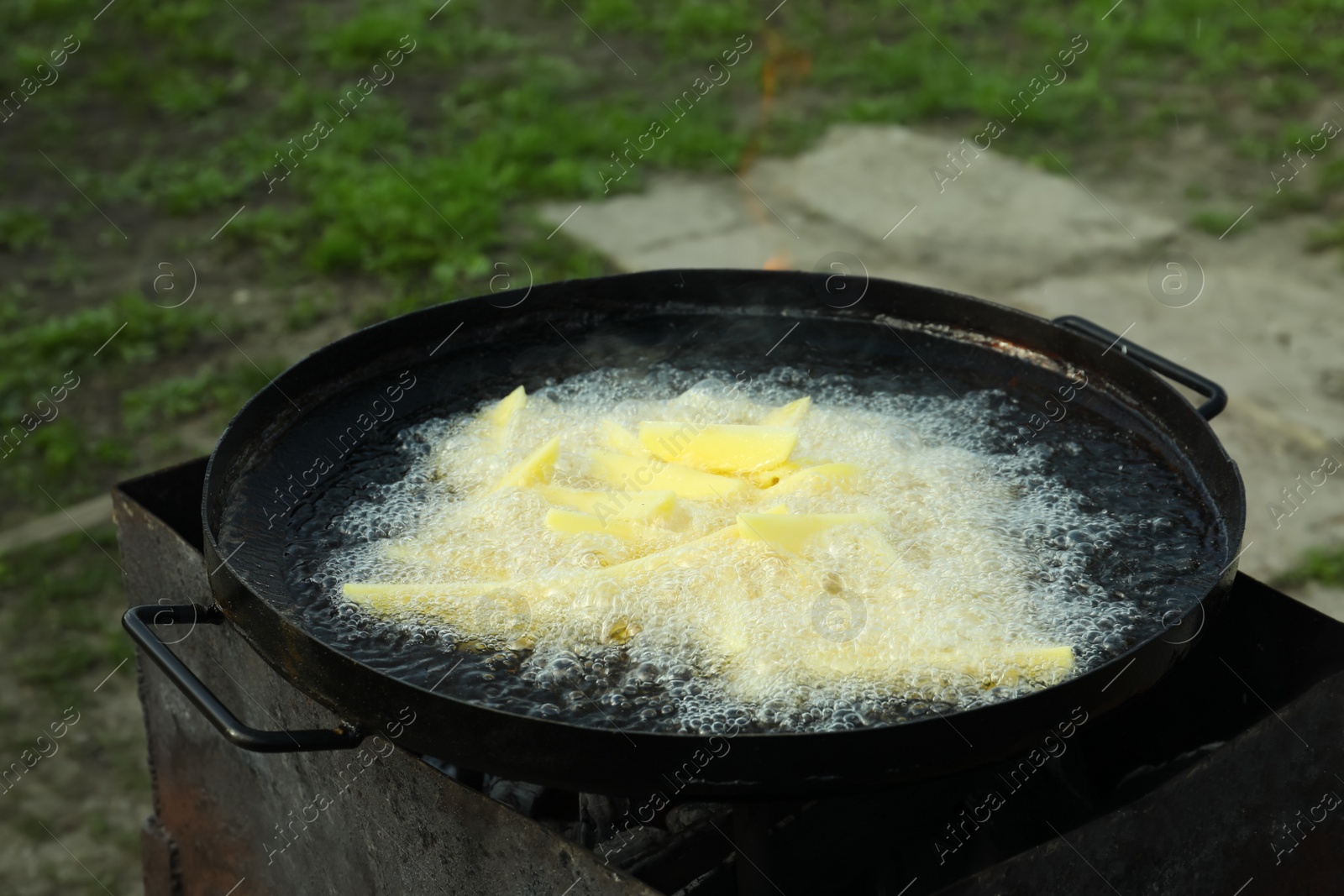 Photo of Cooking delicious potato wedges on frying pan outdoors