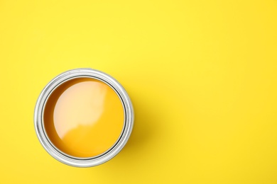 Photo of Open can of paint on yellow background, top view. Space for text
