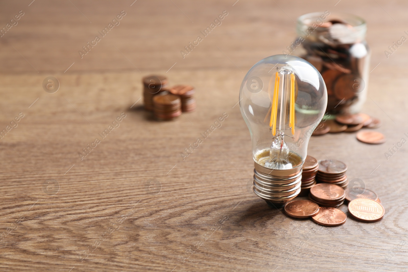 Photo of Lamp bulb and coins on wooden table, space for text. Money saving concept