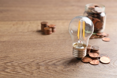 Lamp bulb and coins on wooden table, space for text. Money saving concept