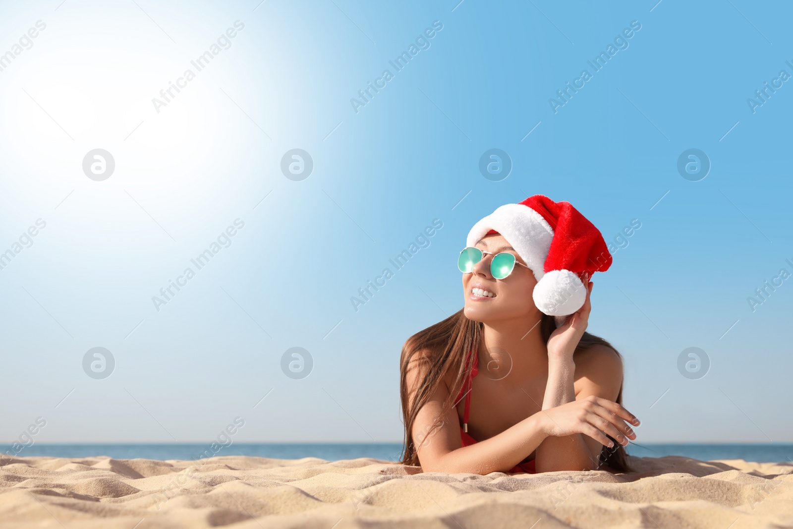 Photo of Beautiful young woman in Santa hat and bikini on beach, space for text. Christmas vacation