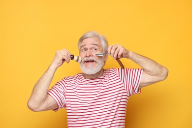 Photo of Senior man with mustache holding blade and brush on orange background