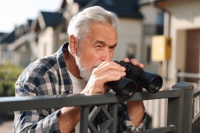 Photo of Concept of private life. Curious senior man with binoculars spying on neighbours over fence outdoors