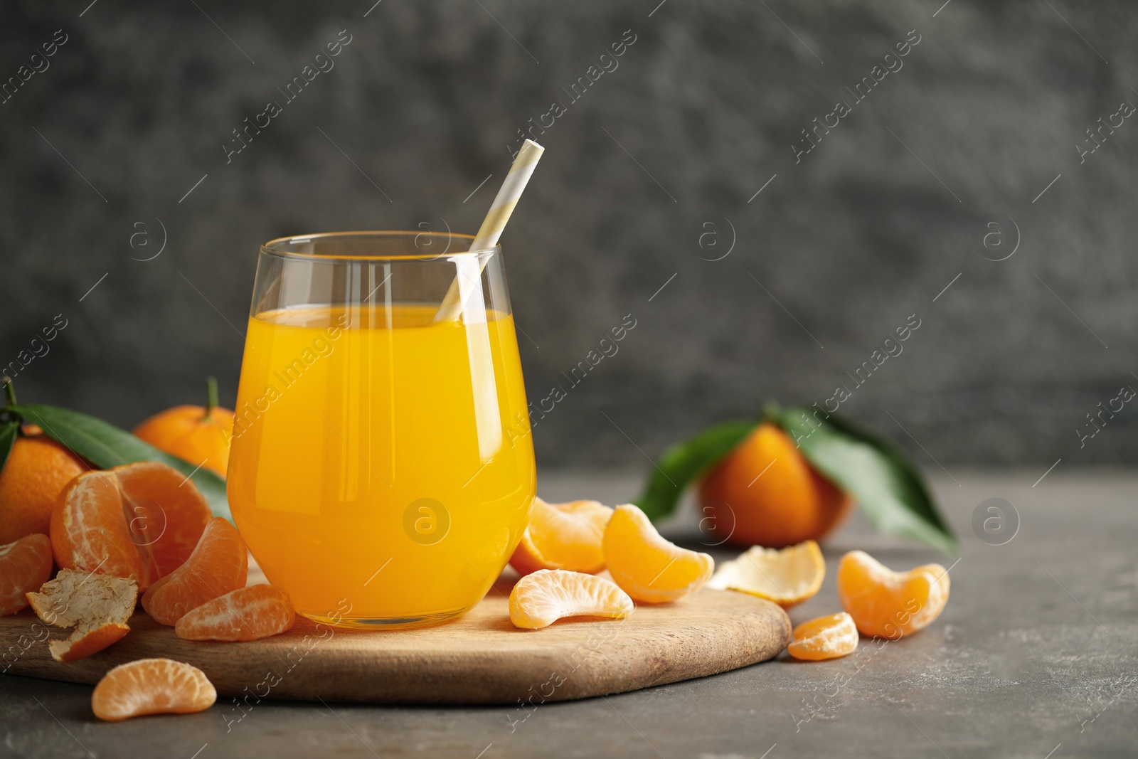 Photo of Fresh tangerines and glass of juice on grey table. Space for text