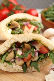 Delicious pita sandwiches with cheese, mushrooms tomatoes and arugula on wooden table, closeup