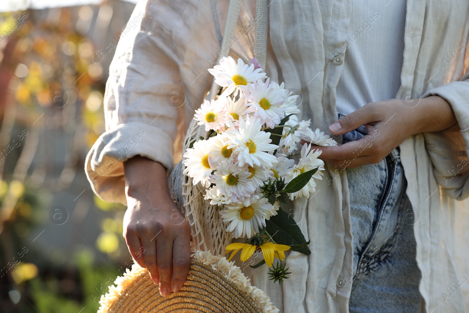 Photo of Woman holding net bag of beautiful white chamomile flowers outdoors, closeup