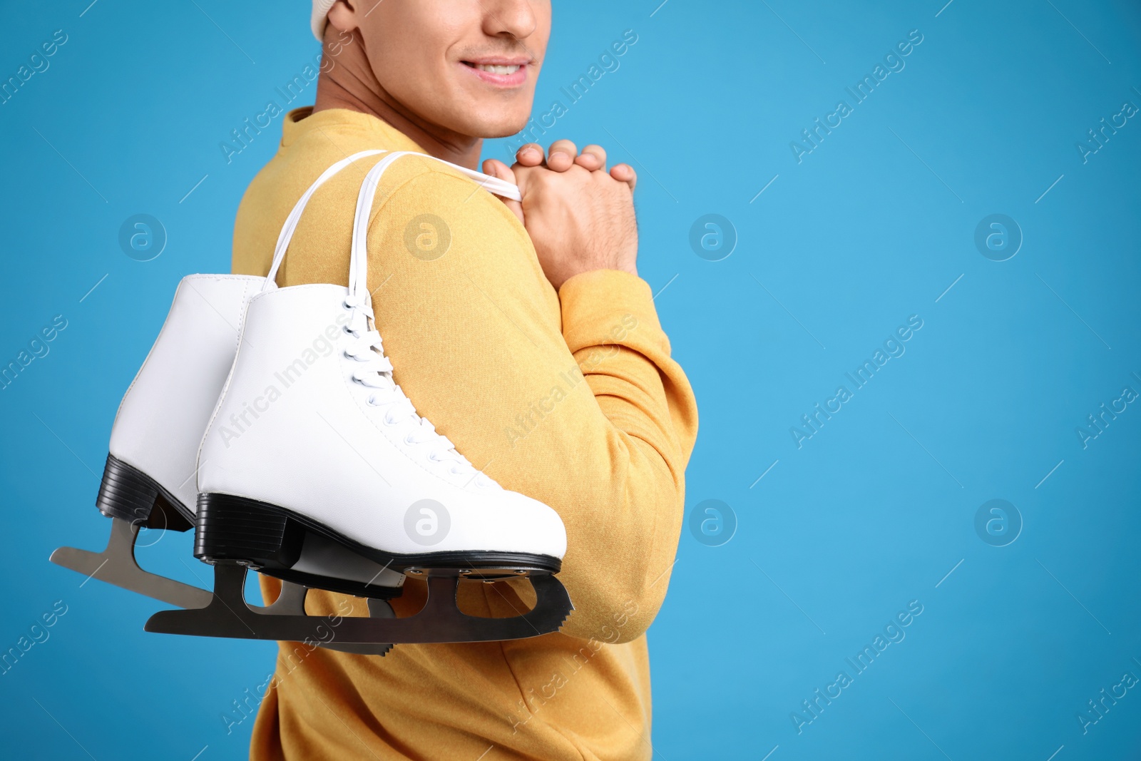 Photo of Happy man with ice skates on light blue background, closeup. Space for text