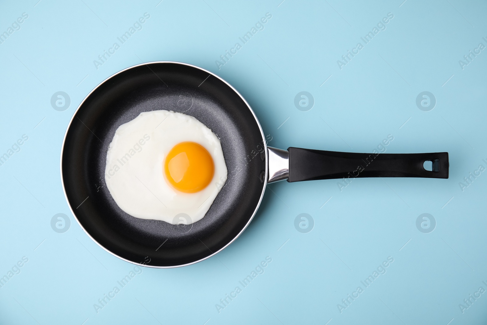 Photo of Tasty fried egg in pan on light blue background, top view