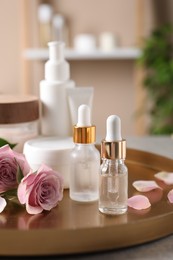 Bottles of cosmetic serum, beauty products and flowers on table indoors