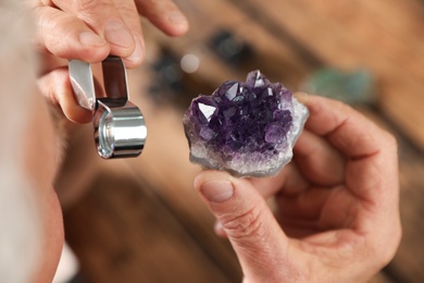 Photo of Male jeweler evaluating semi precious gemstone at table in workshop, closeup