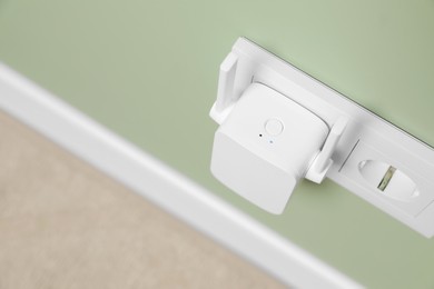 Wireless Wi-Fi repeater on light green wall indoors, above view