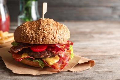 Photo of Tasty burger with bacon on wooden table