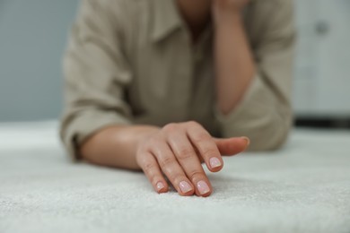 Woman touching soft white carpet indoors, closeup