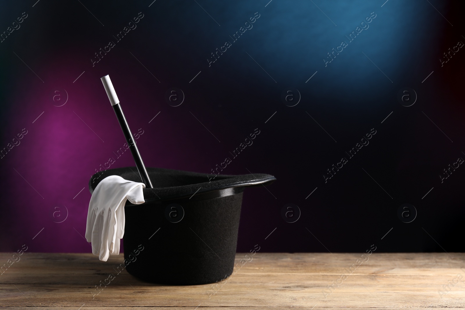 Photo of Magician's hat, gloves and wand on wooden table against dark background, space for text