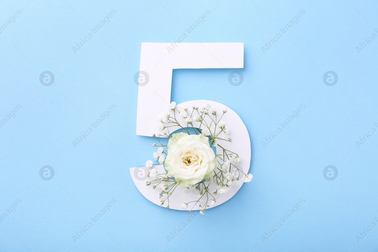 Photo of Paper number 5 and beautiful flowers on light blue background, top view