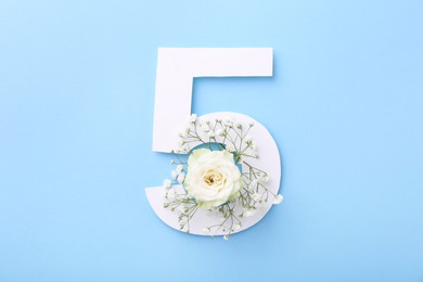 Paper number 5 and beautiful flowers on light blue background, top view