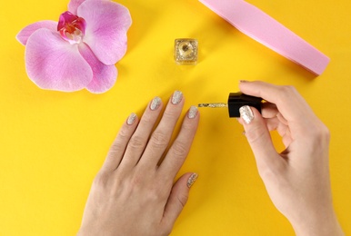 Woman applying nail polish on color background, top view