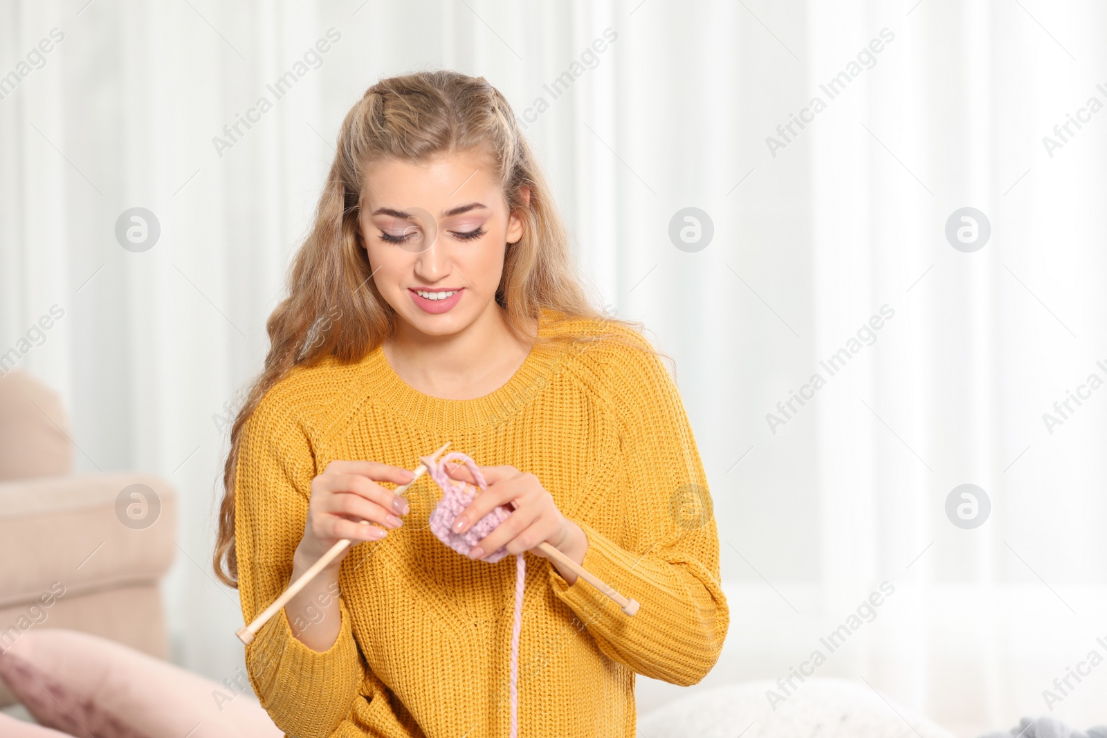 Photo of Young woman in cozy warm sweater knitting with needles at home. Space for text