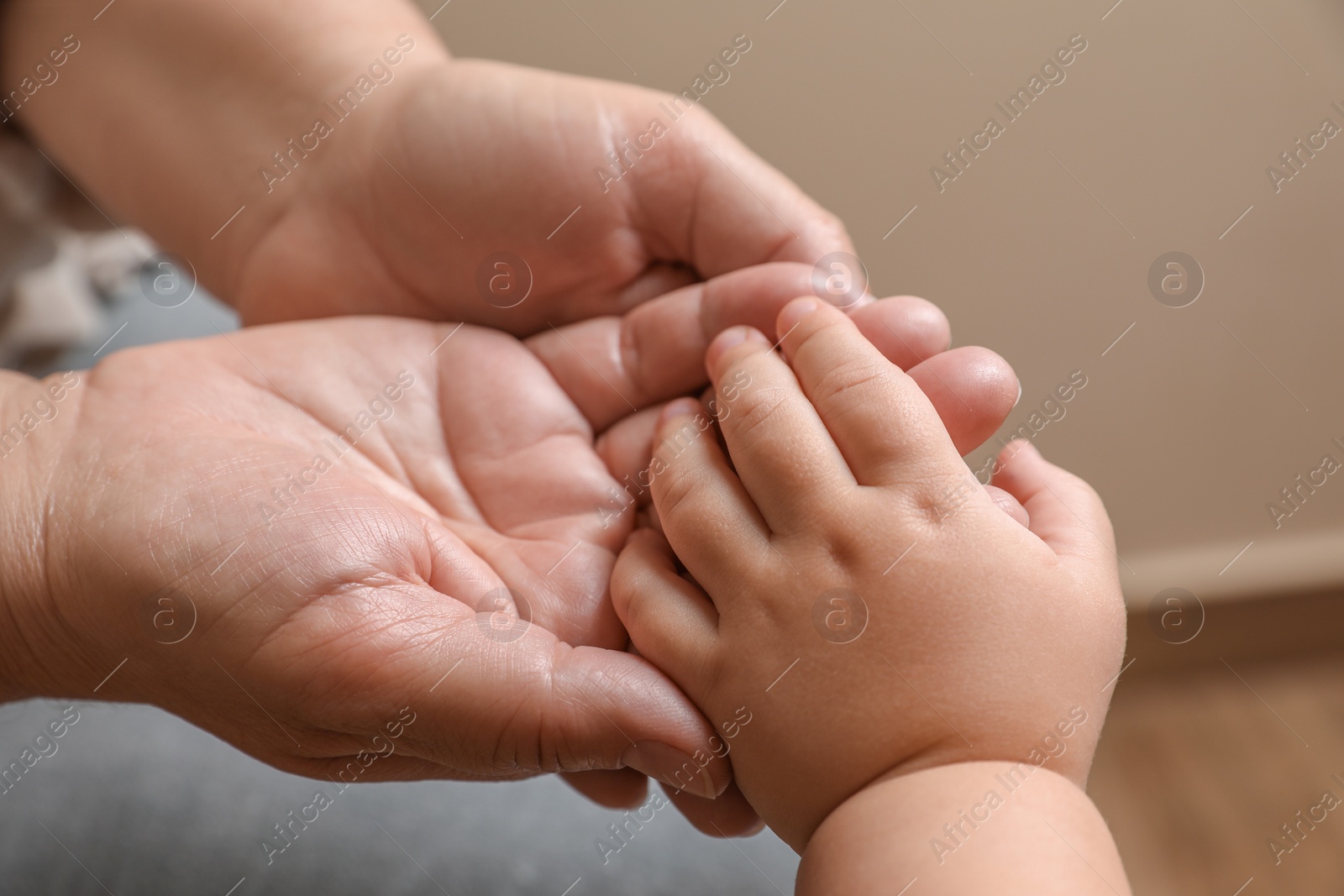 Photo of Woman holding hands with her granddaughter on beige background, closeup