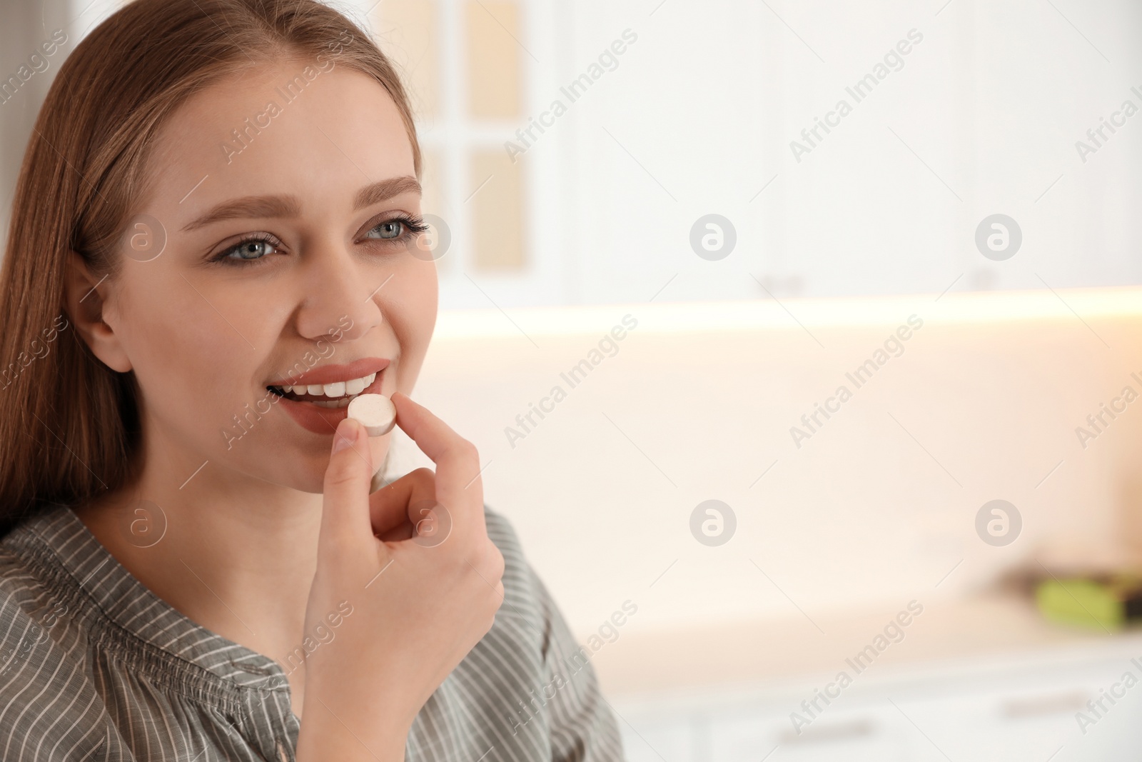 Photo of Young woman taking vitamin pill on light background. Space for text