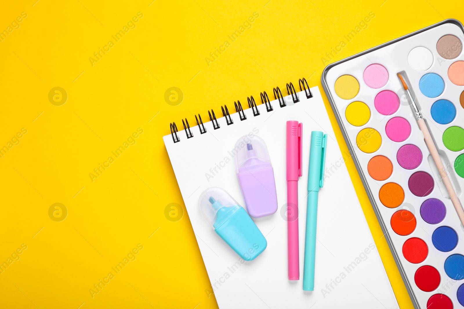 Photo of Watercolor palette, notebook and colorful markers on yellow background, flat lay. Space for text