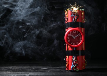 Photo of Dynamite time bomb on wooden table against black background. Space for text