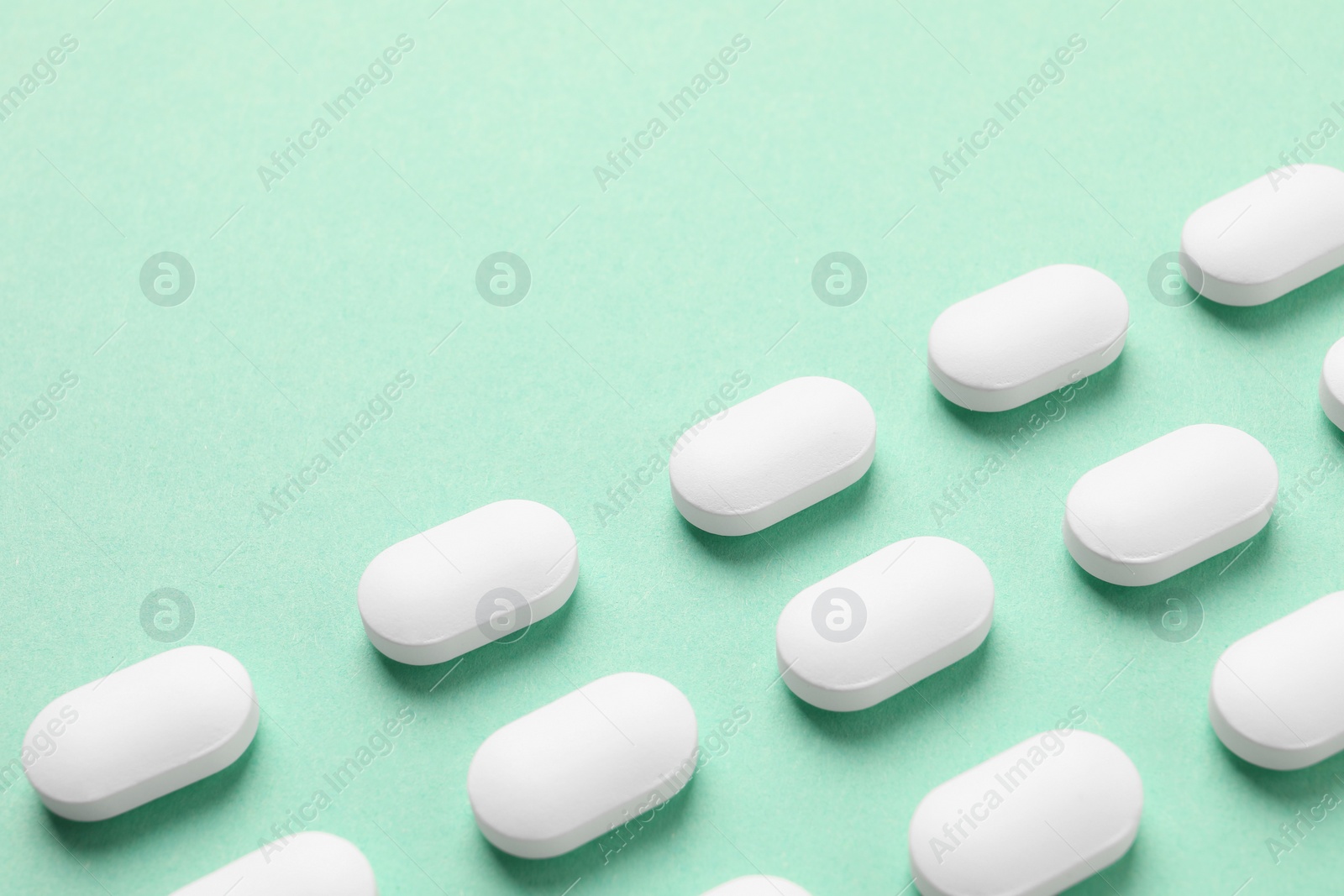 Photo of Many white pills on green background, space for text