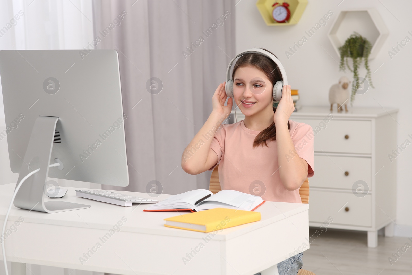 Photo of Cute girl using computer and headphones at desk in room. Home workplace