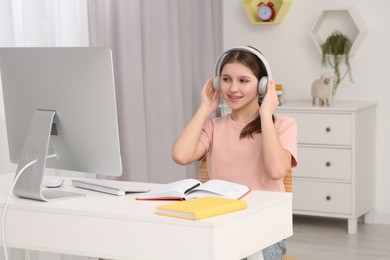 Photo of Cute girl using computer and headphones at desk in room. Home workplace