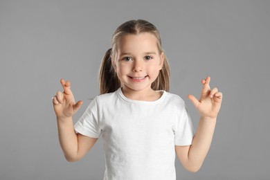 Photo of Child with crossed fingers on light grey background. Superstition concept