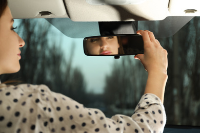 Photo of Young woman adjusting rear view mirror in car, closeup