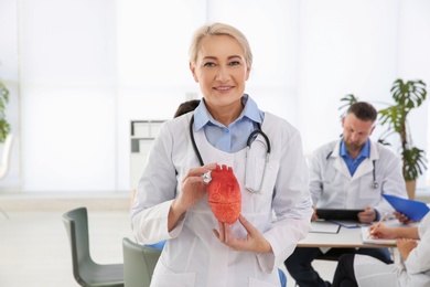 Photo of Female doctor holding heart model in clinic. Cardiology center