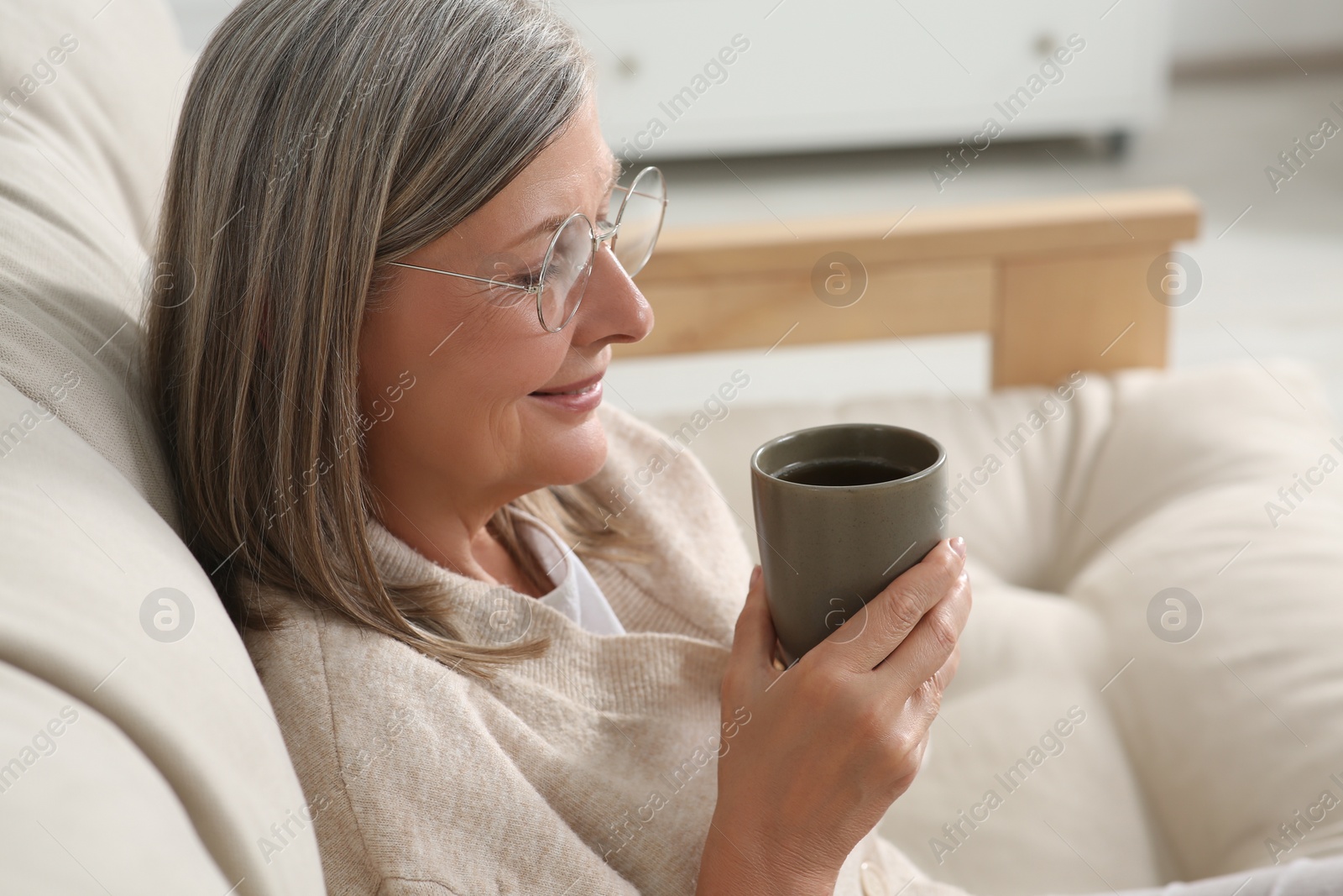 Photo of Beautiful senior woman drinking tea on sofa at home