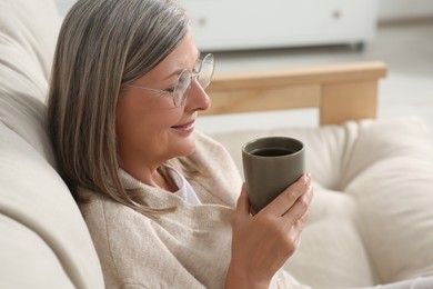 Beautiful senior woman drinking tea on sofa at home