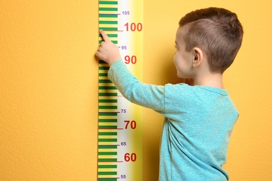 Photo of Little boy measuring his height on color background