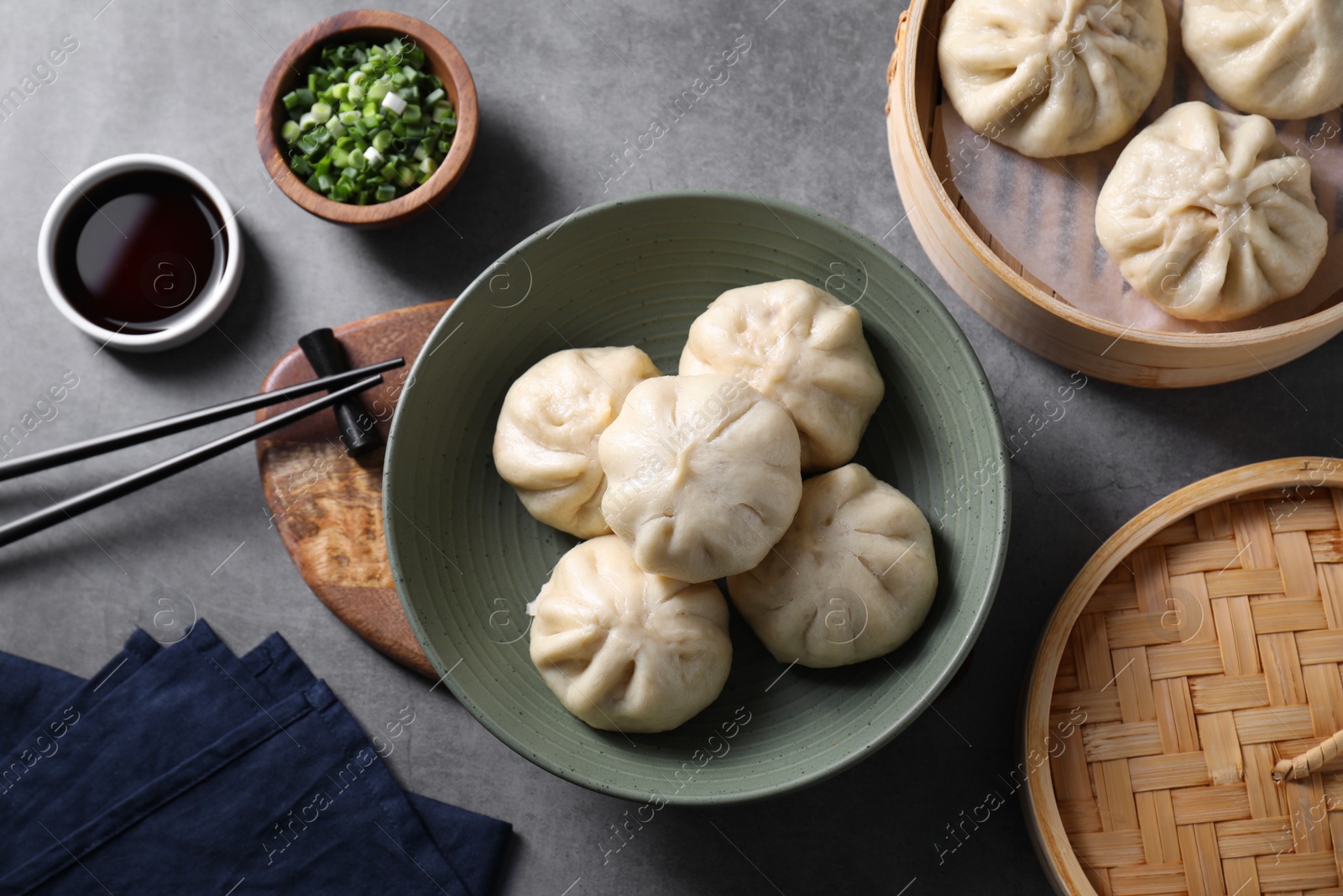 Photo of Delicious bao buns (baozi), chopsticks, soy sauce and green onion on grey table, flat lay