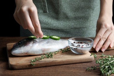 Photo of Woman sprinkling dorado fish with seasoning at wooden table, closeup