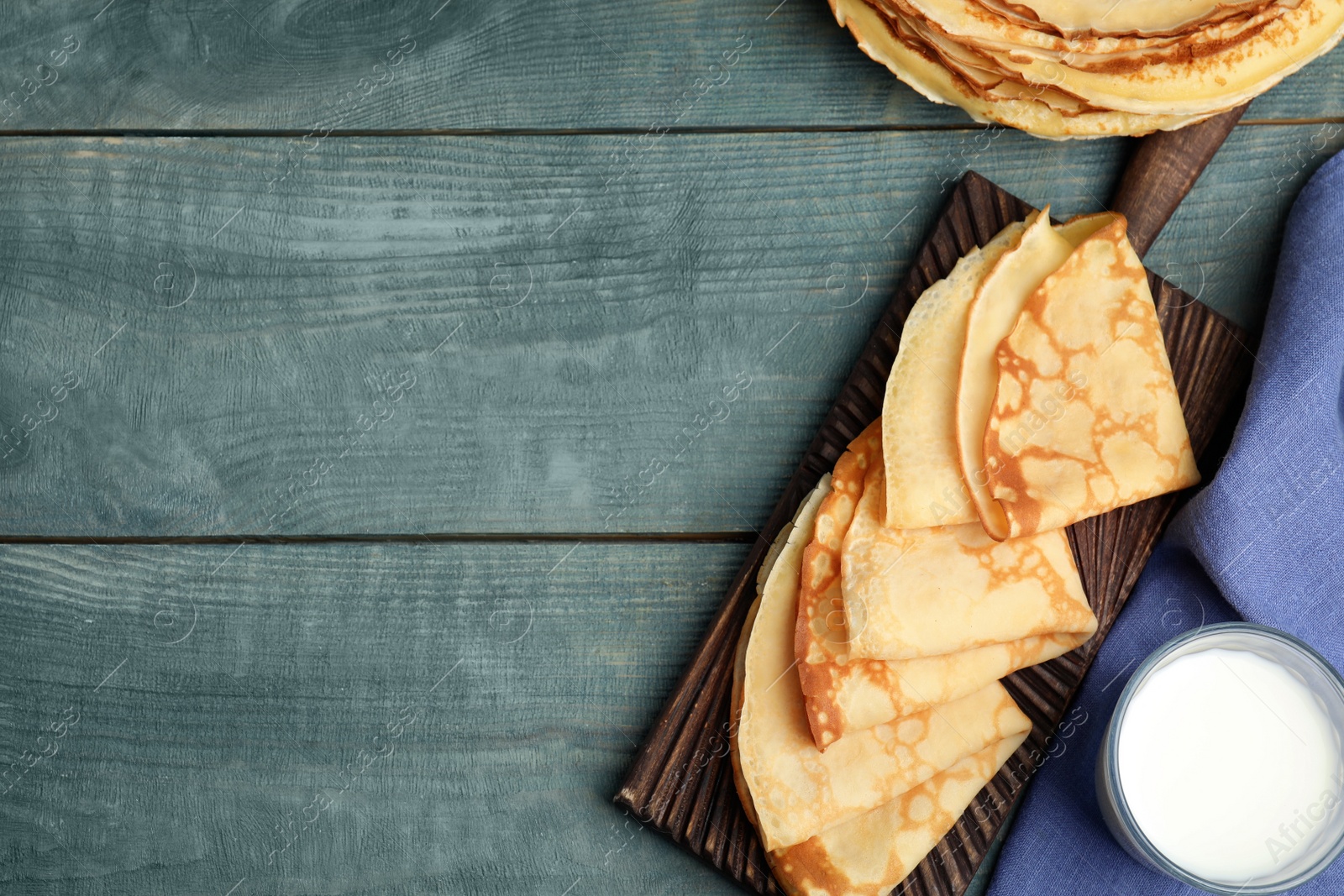 Photo of Flat lay composition with fresh thin pancakes on blue wooden table. Space for text