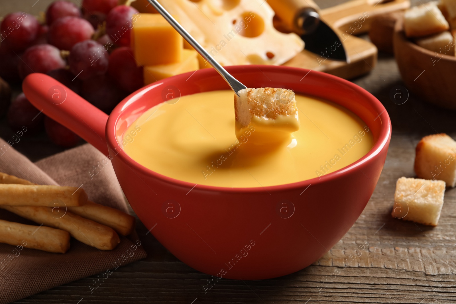 Photo of Dipping piece of bread into tasty cheese fondue at wooden table, closeup