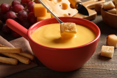 Dipping piece of bread into tasty cheese fondue at wooden table, closeup