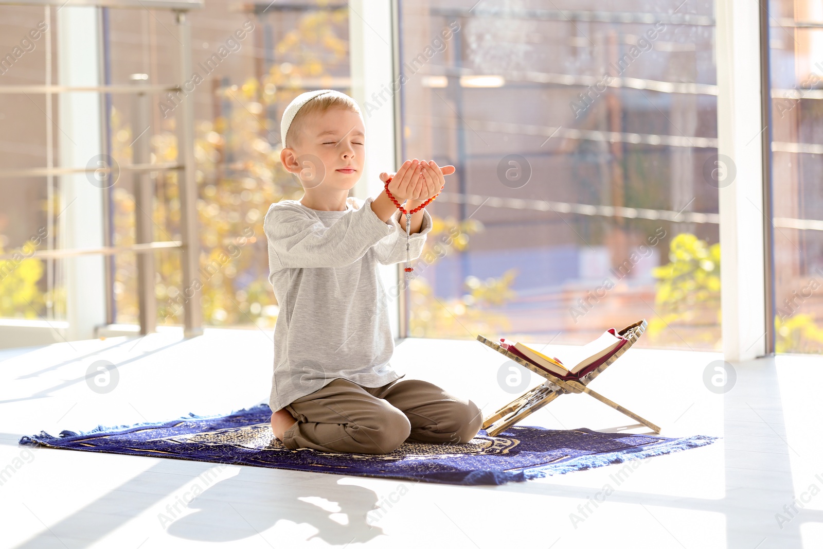 Photo of Little Muslim boy with misbaha and Koran praying on rug indoors