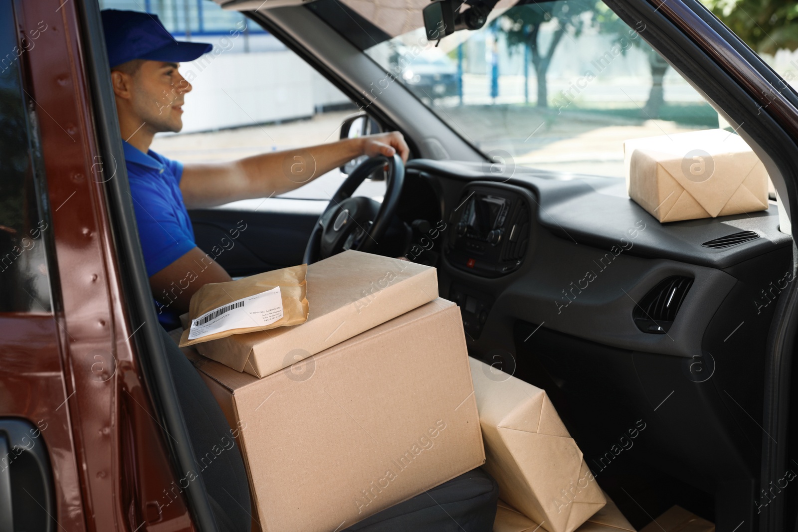 Photo of Young courier with parcels in delivery car