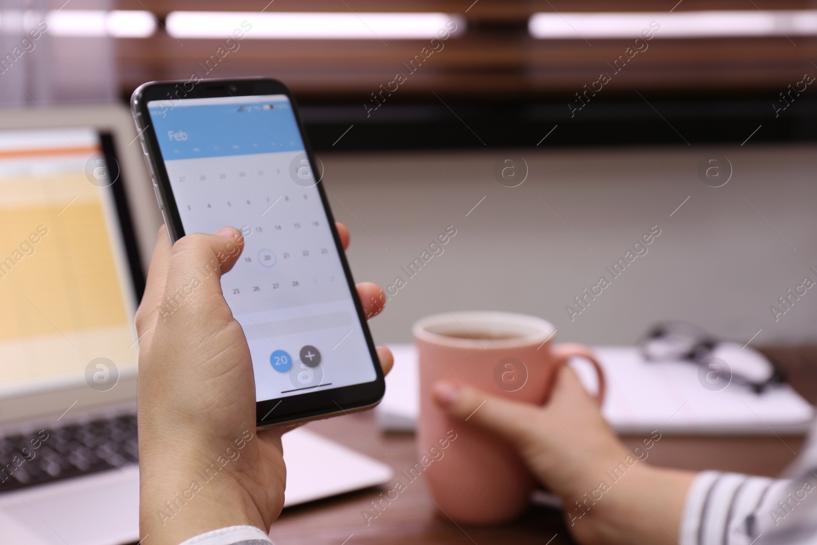 Photo of Woman holding smartphone with calendar app at table, closeup