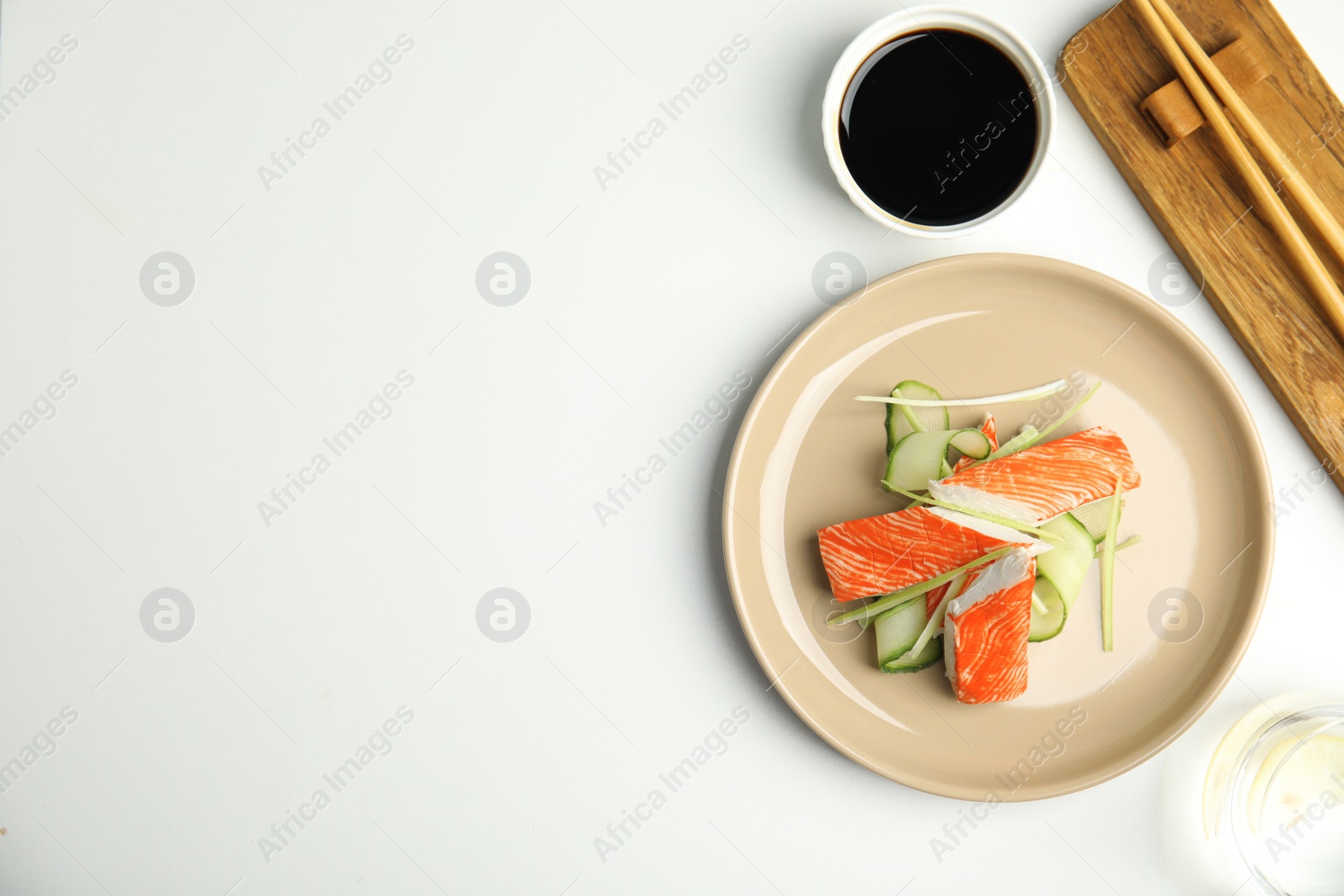 Photo of Fresh crab sticks with cucumber and soy sauce served on white table, flat lay. Space for text