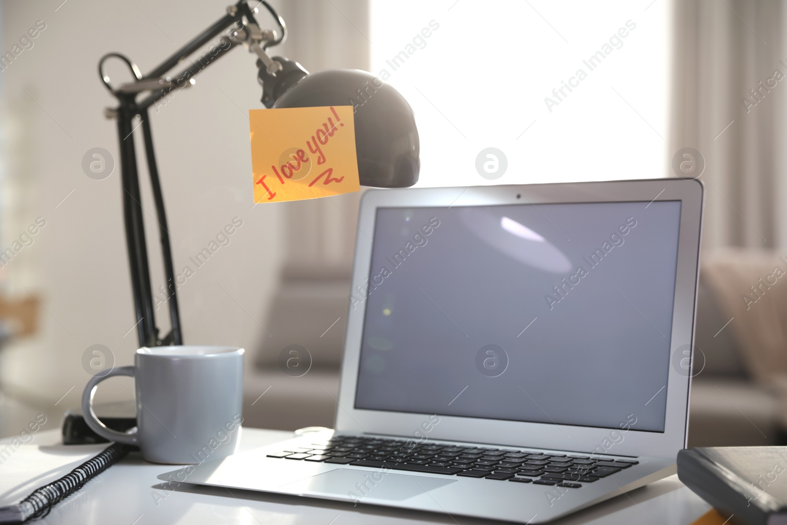 Photo of Sticky note with handwritten text I Love You attached to lamp at workplace. Romantic message