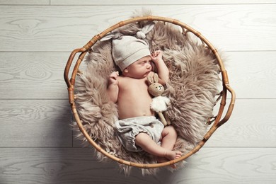 Photo of Cute newborn baby sleeping in wicker basket indoors, top view