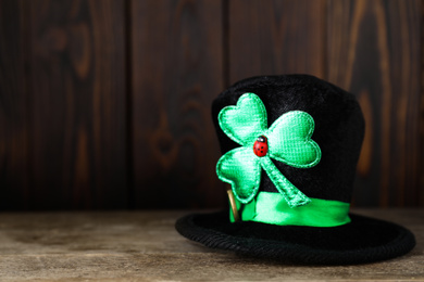 Black leprechaun hat with clover leaf on wooden table, space for text. St. Patrick's Day celebration