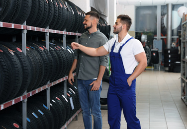 Photo of Mechanic helping client to choose car tire in auto store