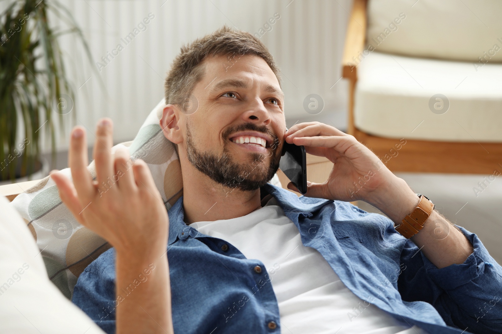 Photo of Smiling man talking on smartphone at home